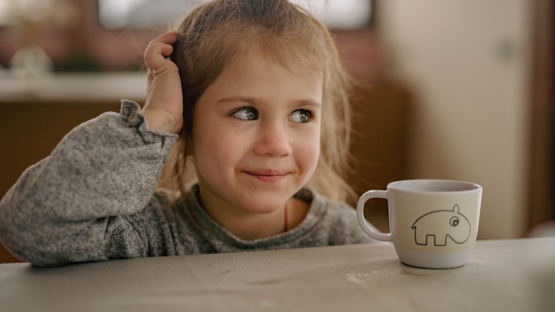 Child sitting at a table with a mug featuring a hippo design.